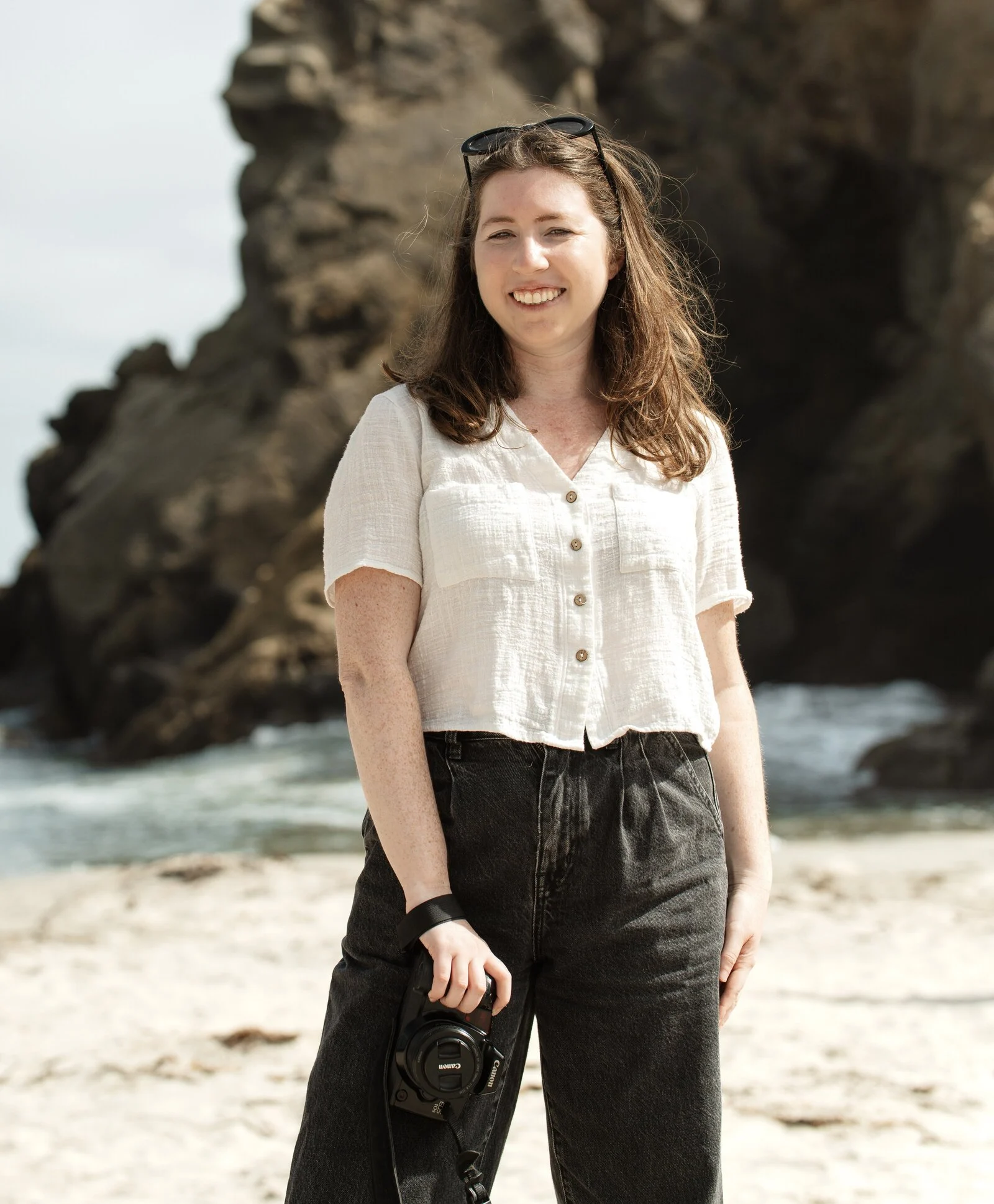 Anna Perlman holding her camera beside coastal rocks