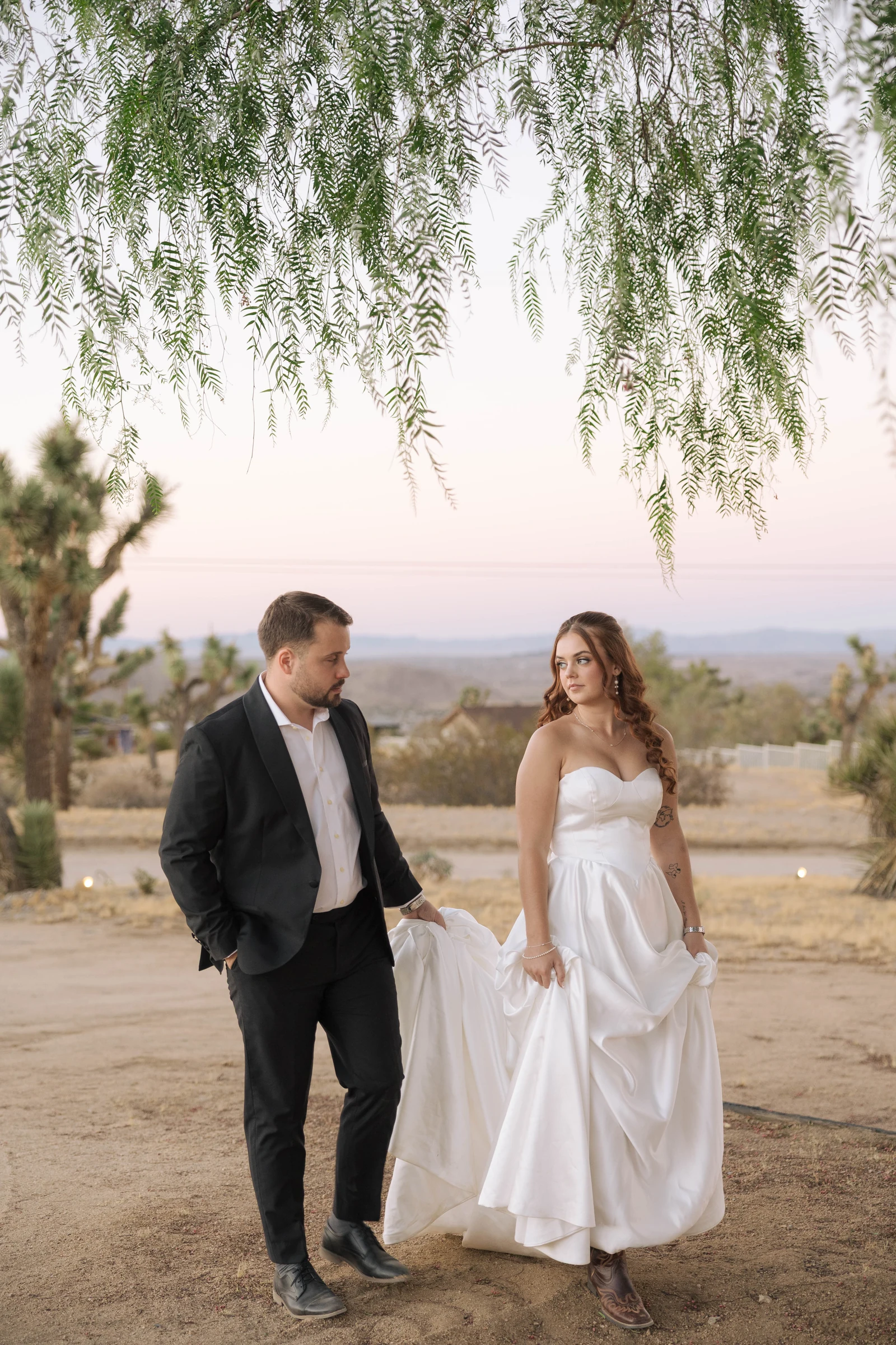 A newly married couple walking together beneath a willow tree at sunset